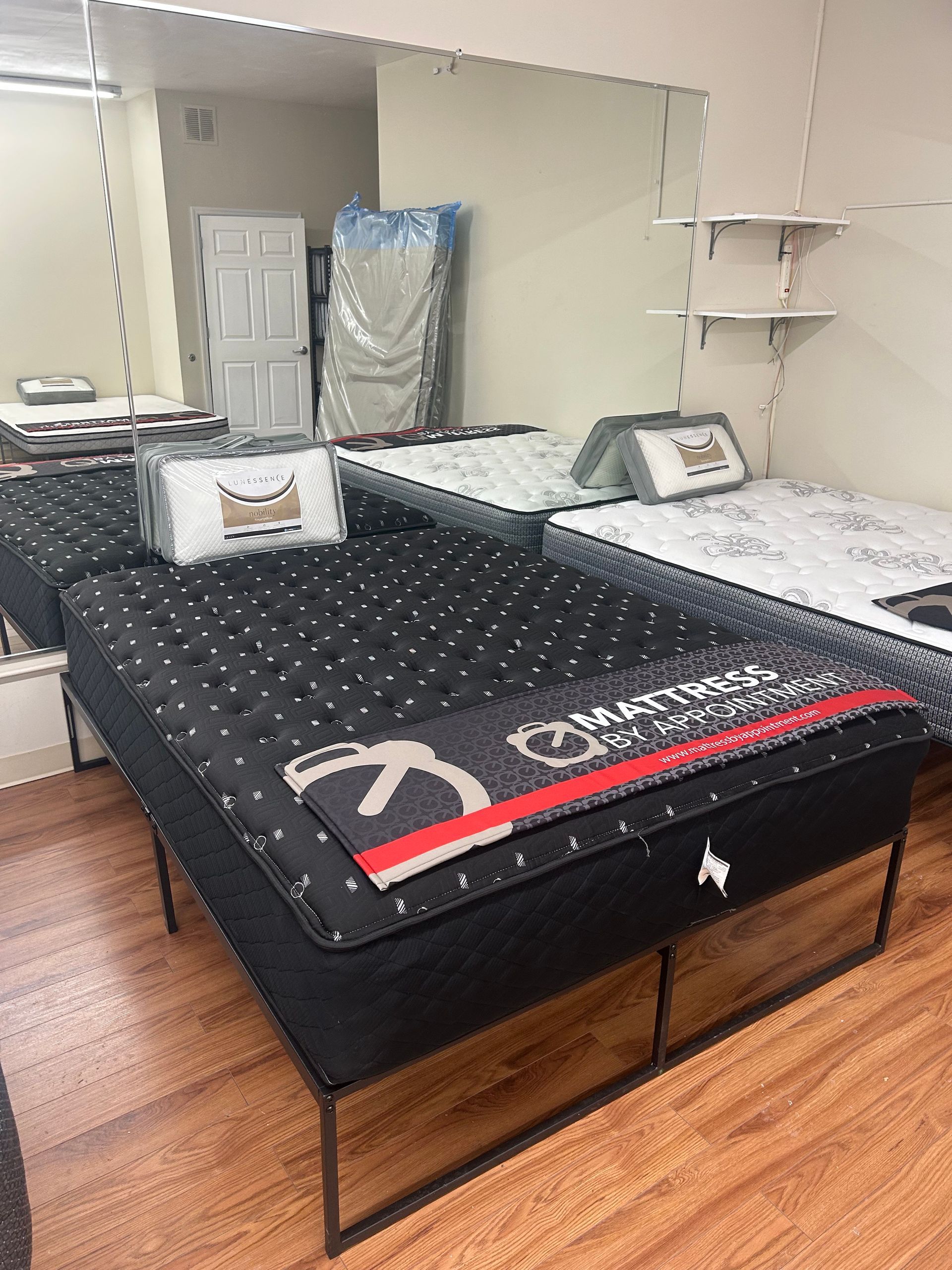 Mattress display in a store, black quilted bed with storage drawers, wood floor, mirrors, and shelving
