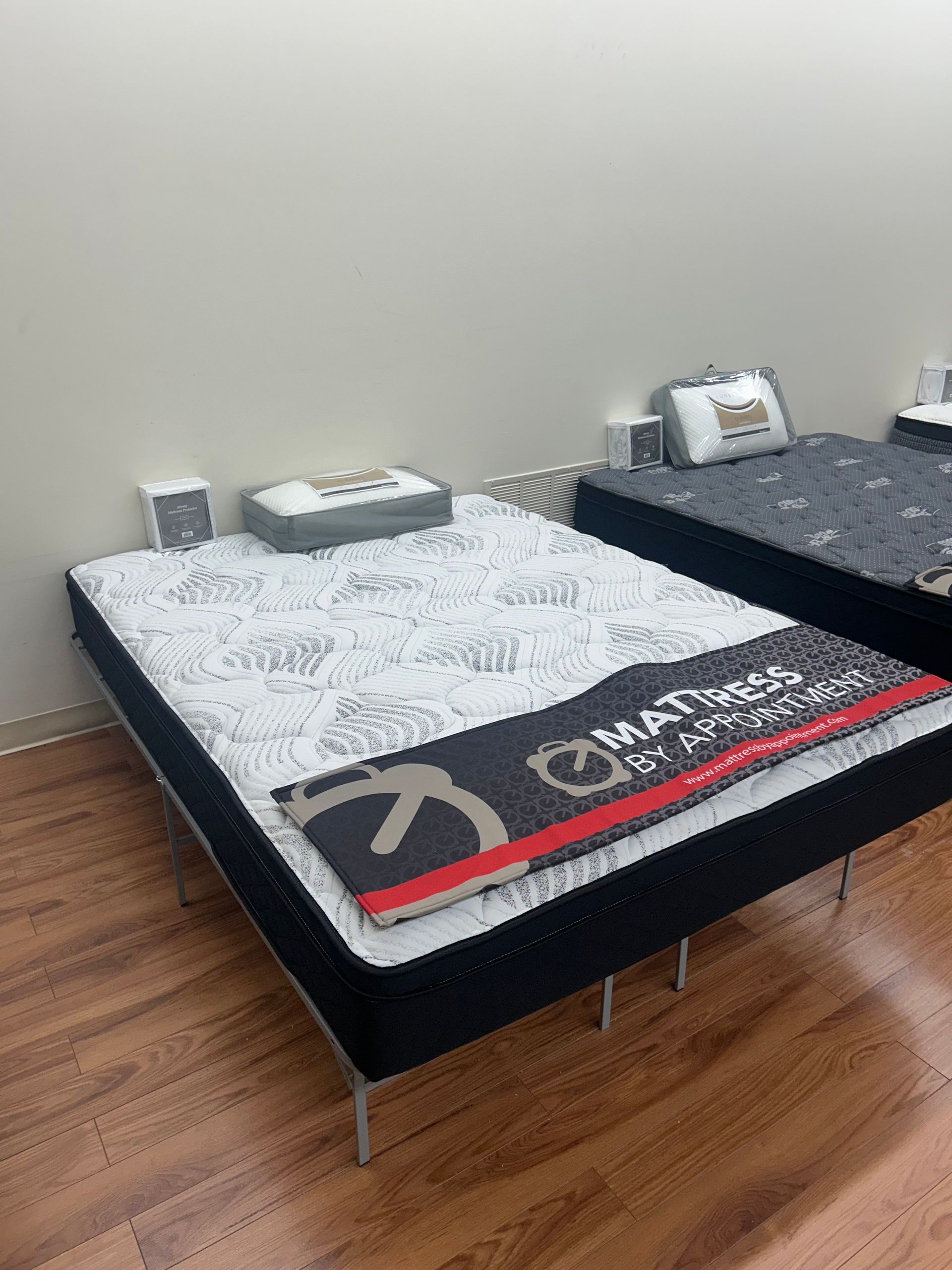 Mattress on a black metal frame, in a retail store setting, with a white and black patterned top