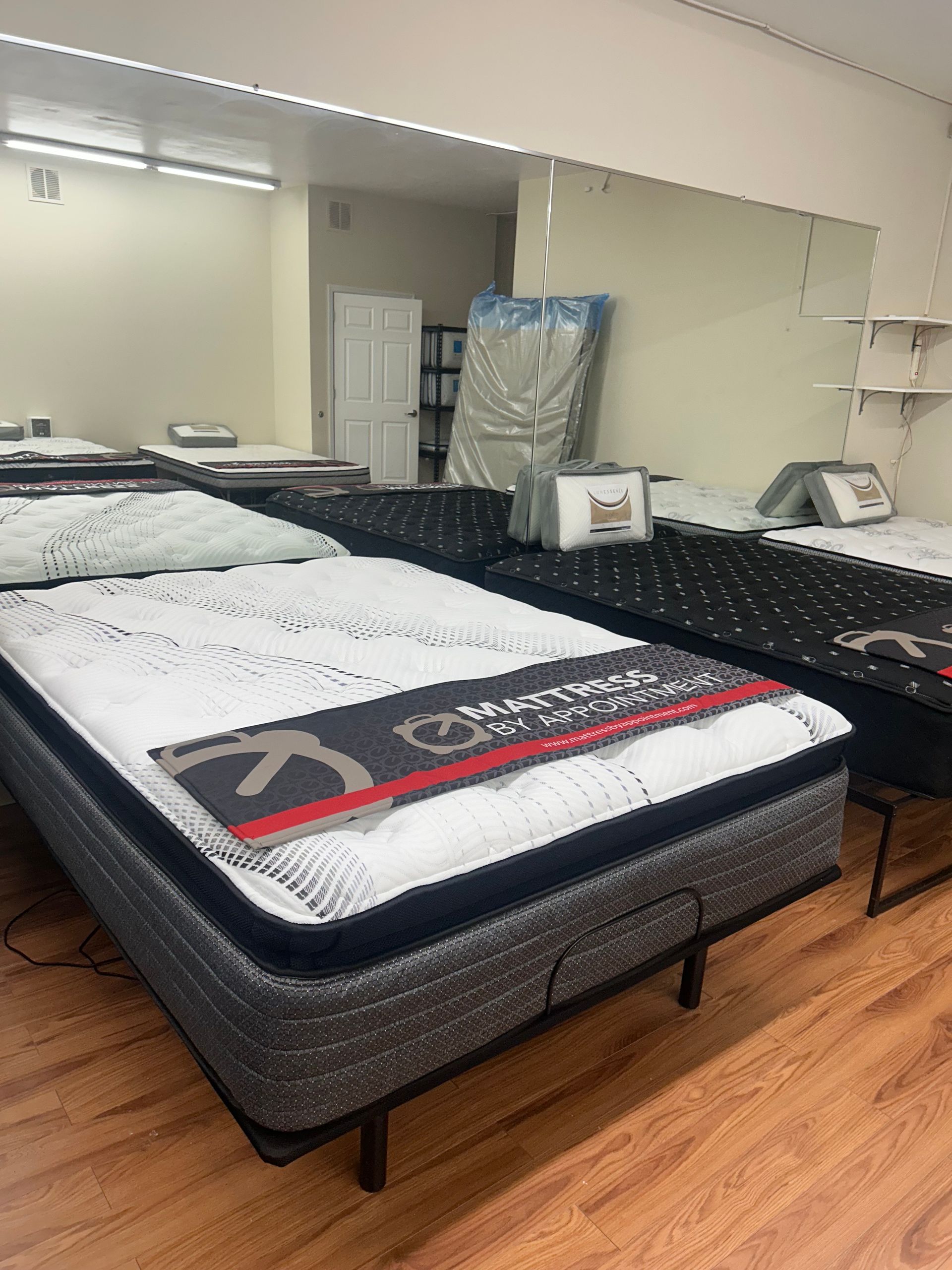 Mattresses displayed in a retail showroom with wood floors and a large mirror