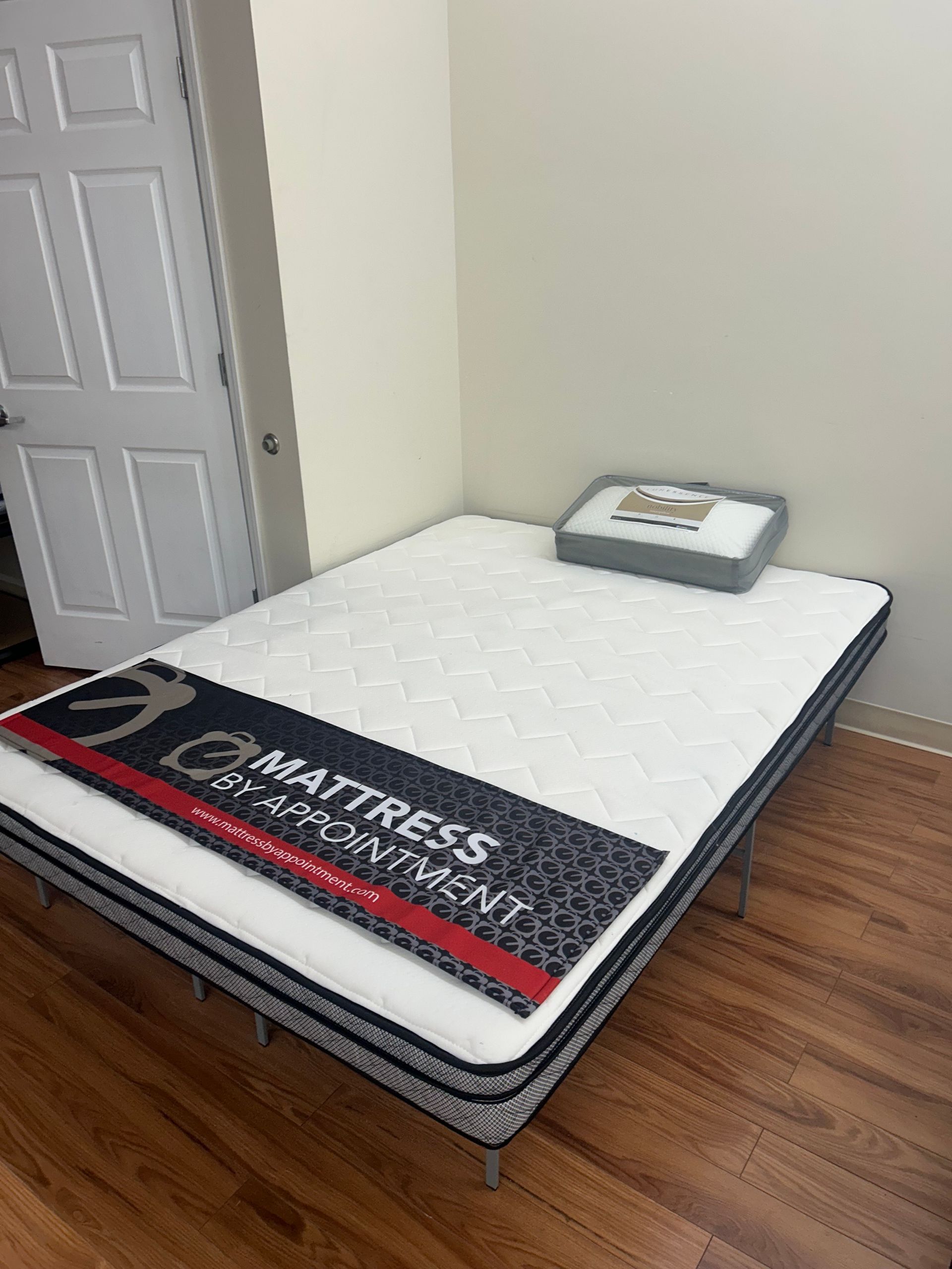 Mattress on a metal frame, in a room with hardwood floors and a closed door