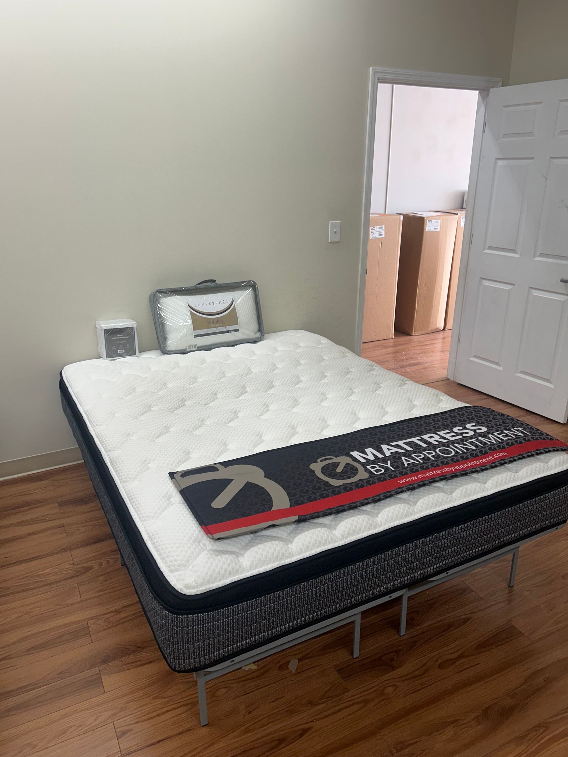 A mattress on a metal frame, in a room with hardwood floors and an open doorway