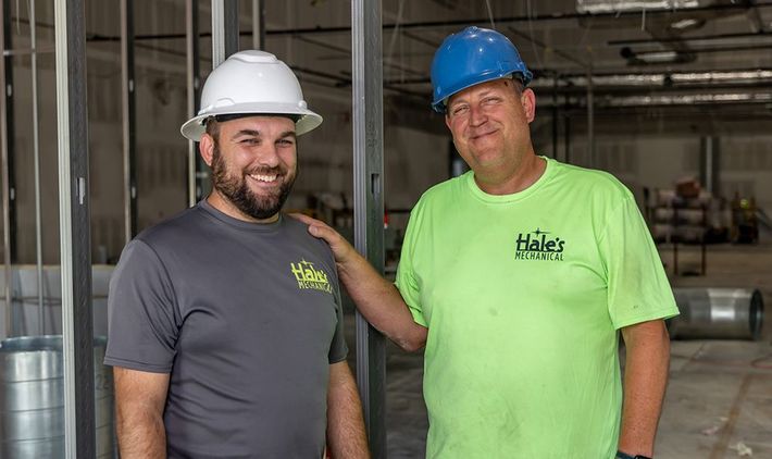 Two construction workers are standing next to each other in a building under construction.
