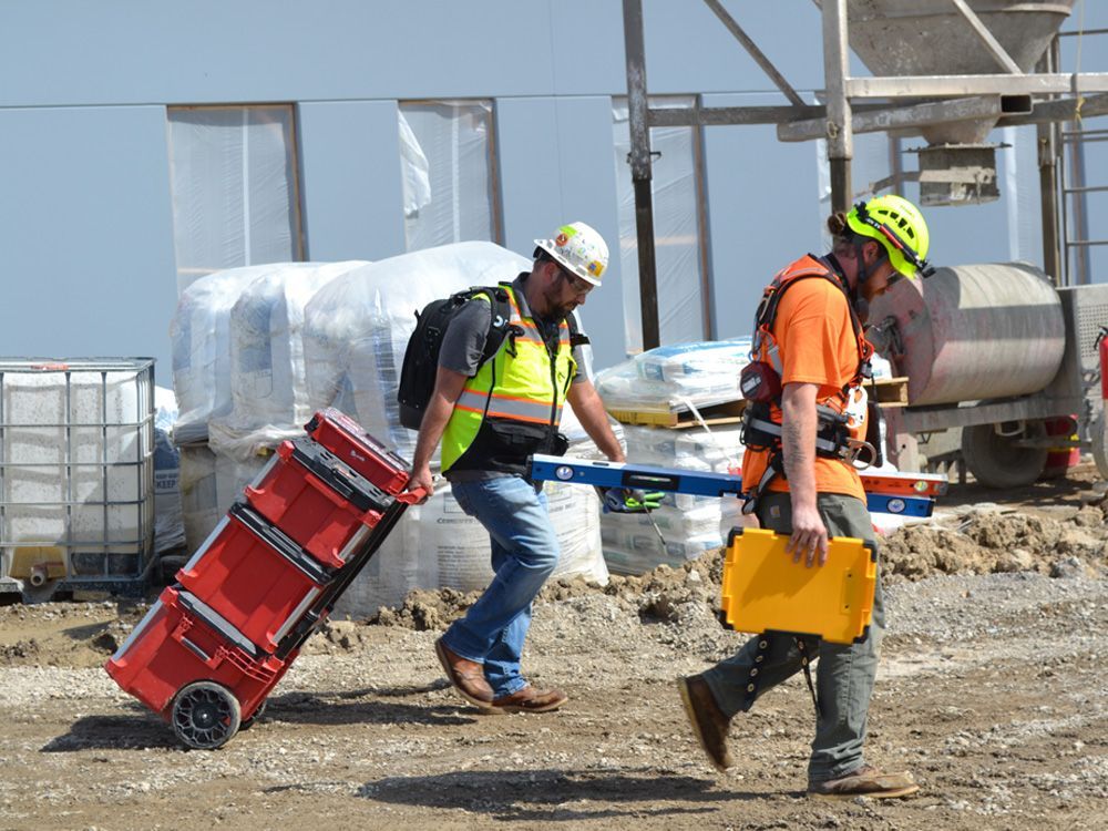 Two construction workers are pushing a red cart on a construction site