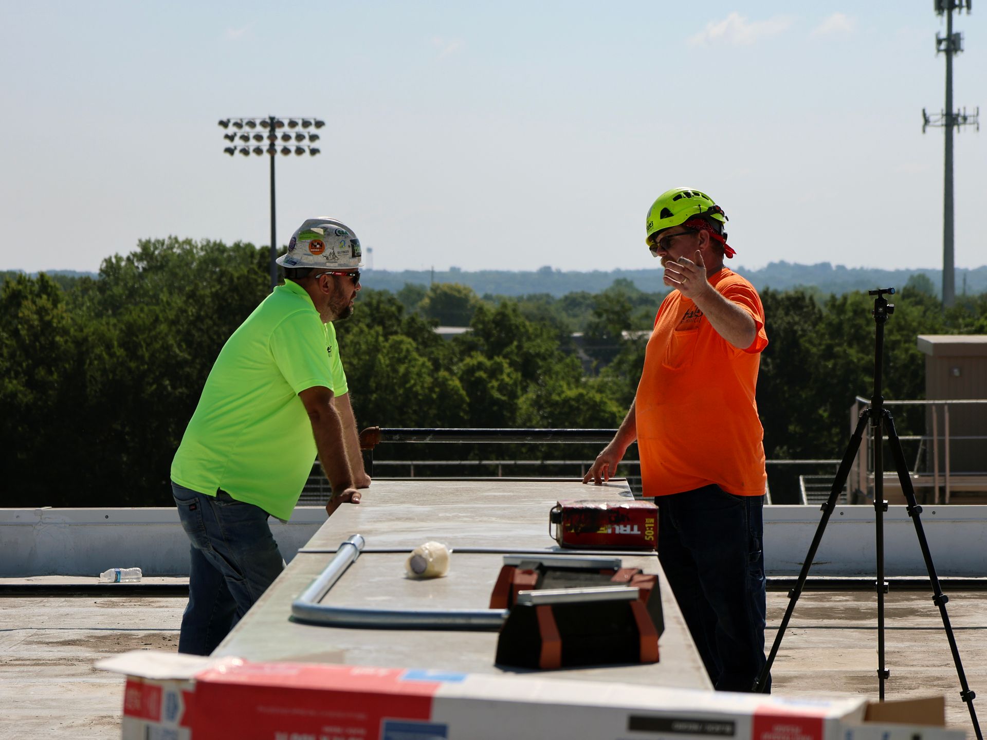 Two construction workers are standing on a roof talking to each other