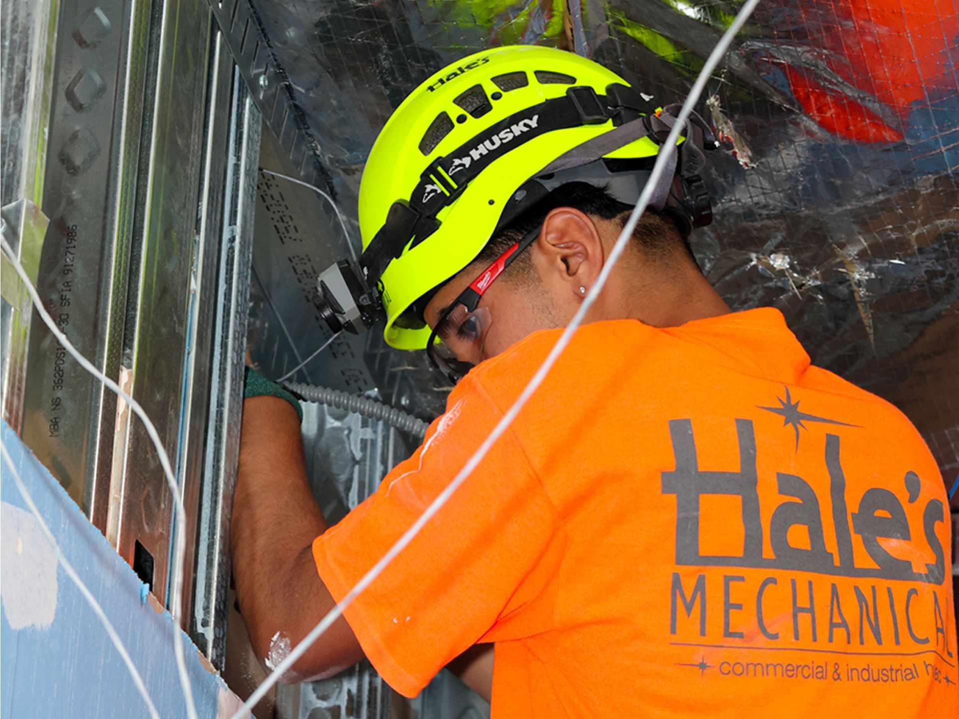 A man wearing a helmet and an orange shirt that says halei mechanics