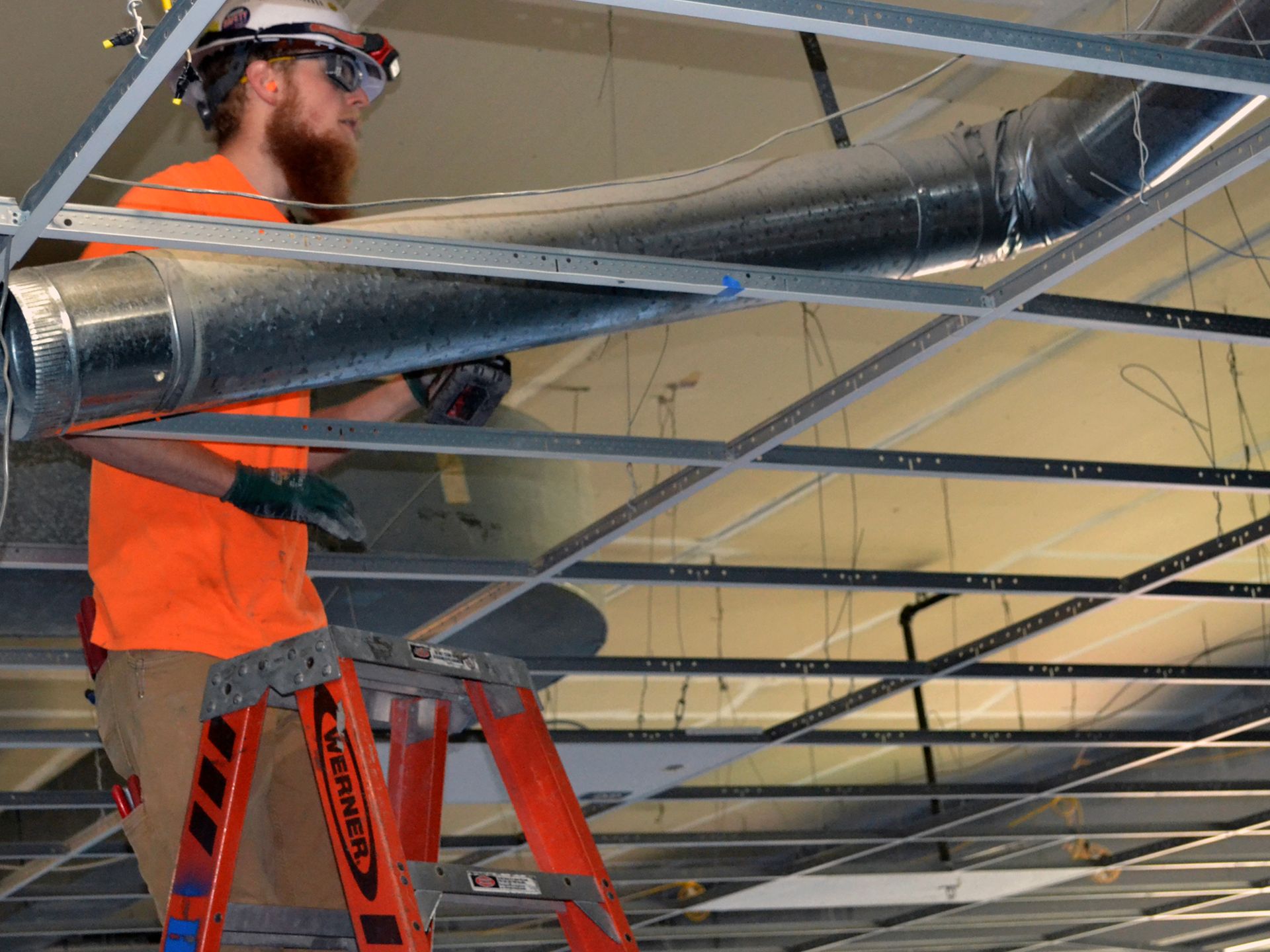 A man is standing on a ladder working on a ceiling.