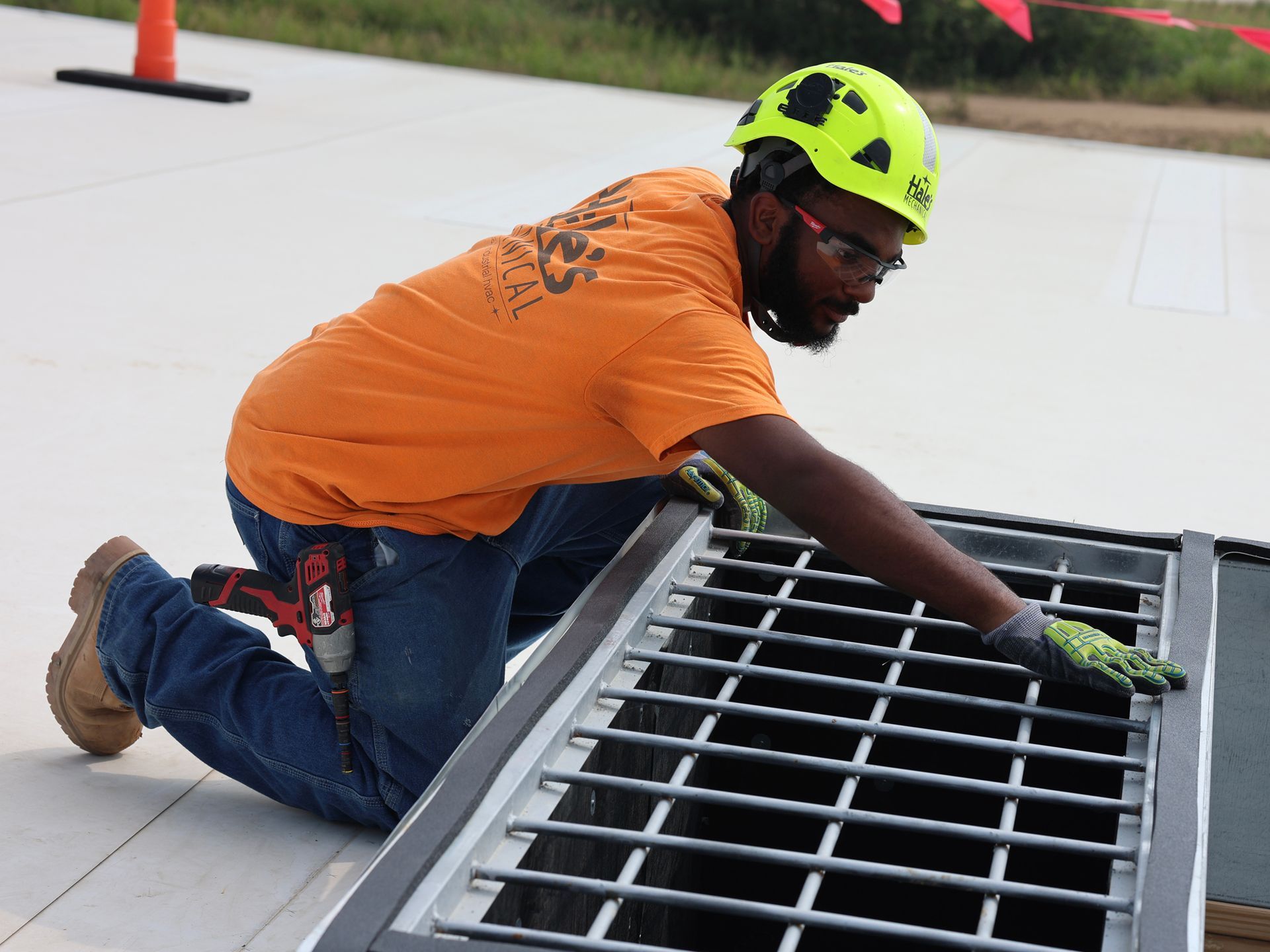 A man wearing an orange shirt and a yellow helmet is working on a manhole cover.