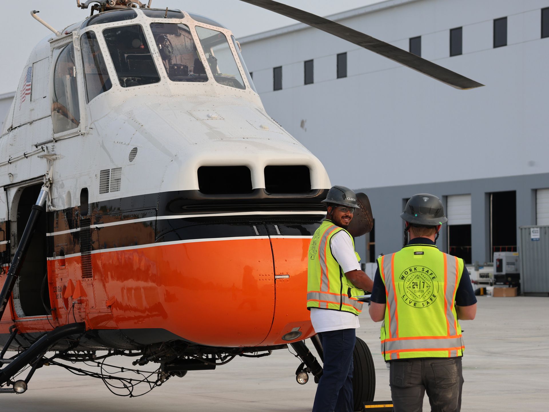 Two men in safety vests are standing in front of a helicopter