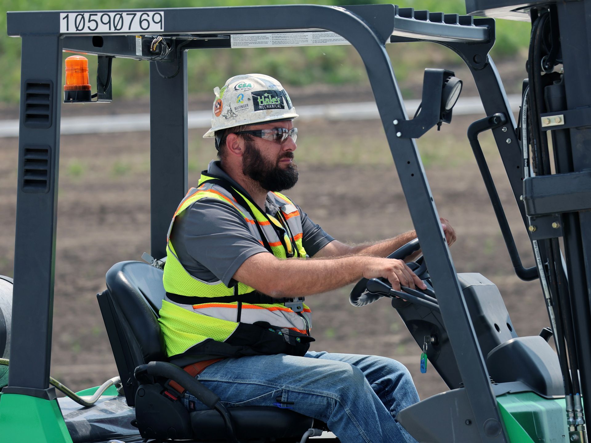 A man wearing a hard hat and safety vest is driving a forklift.