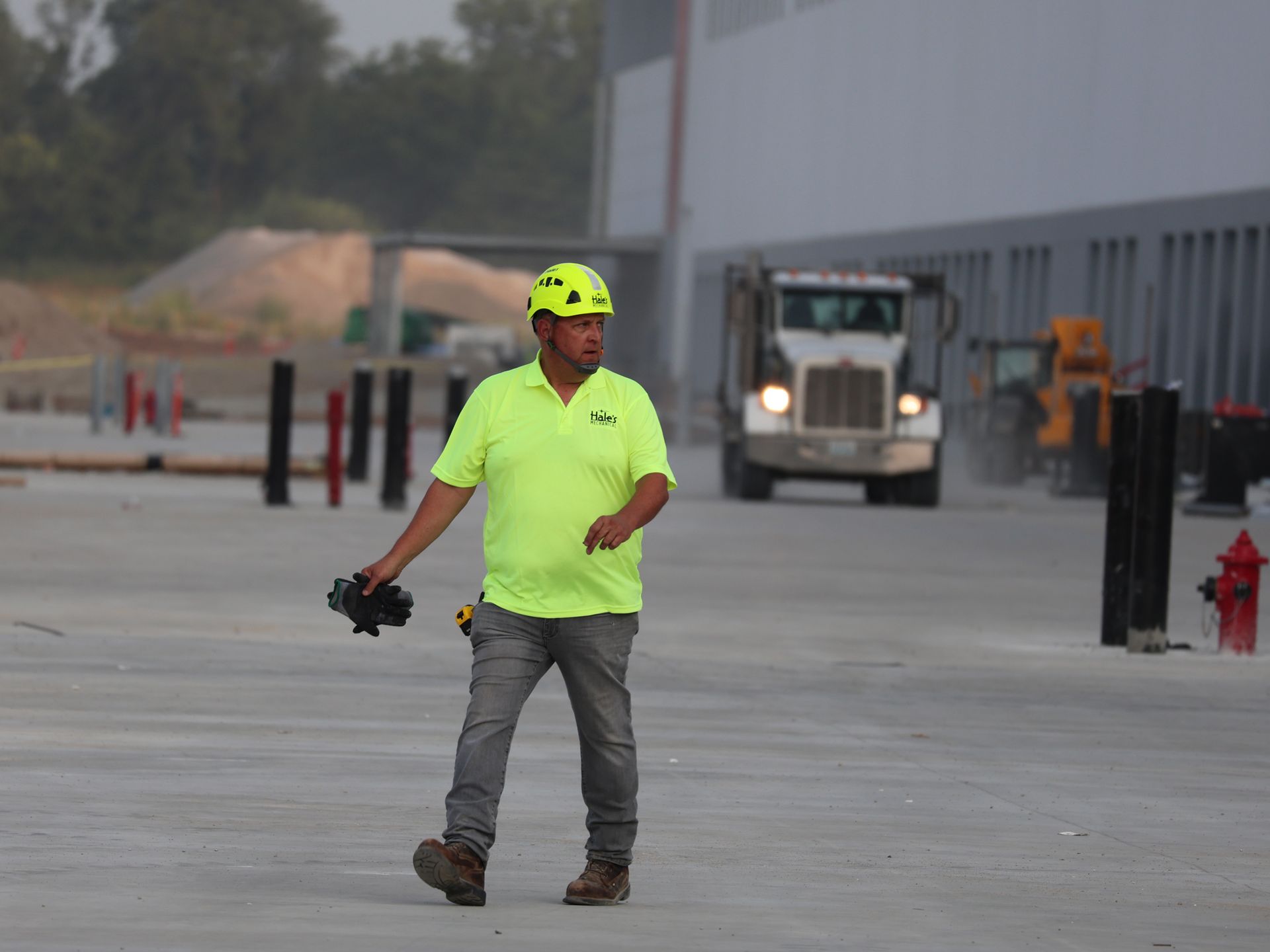 A man wearing a yellow hard hat is walking in front of a truck.