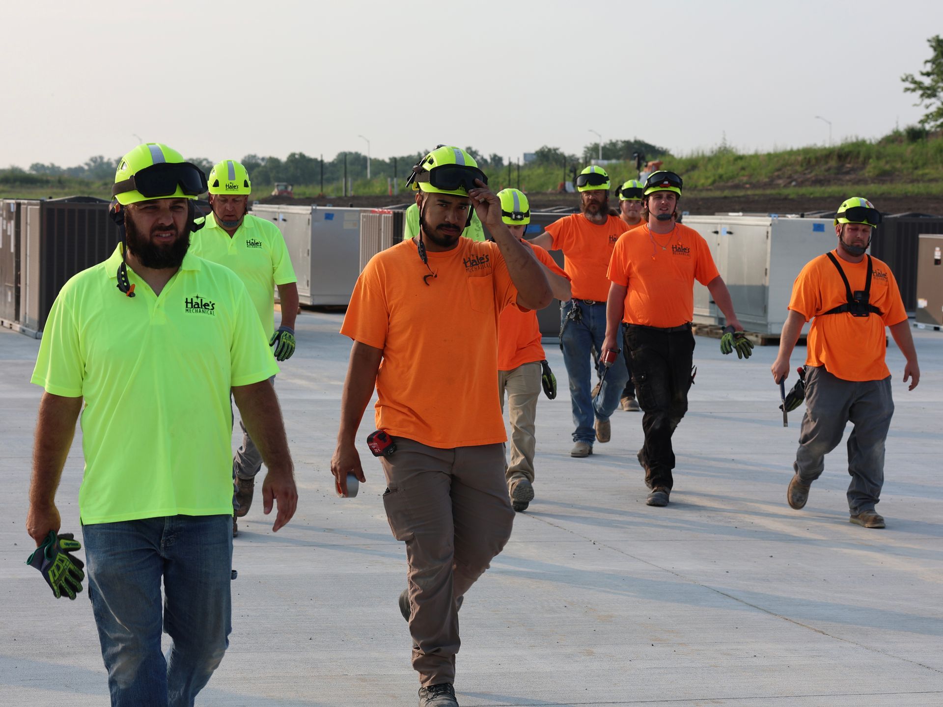 A group of construction workers wearing neon orange shirts and hard hats are walking down a road.