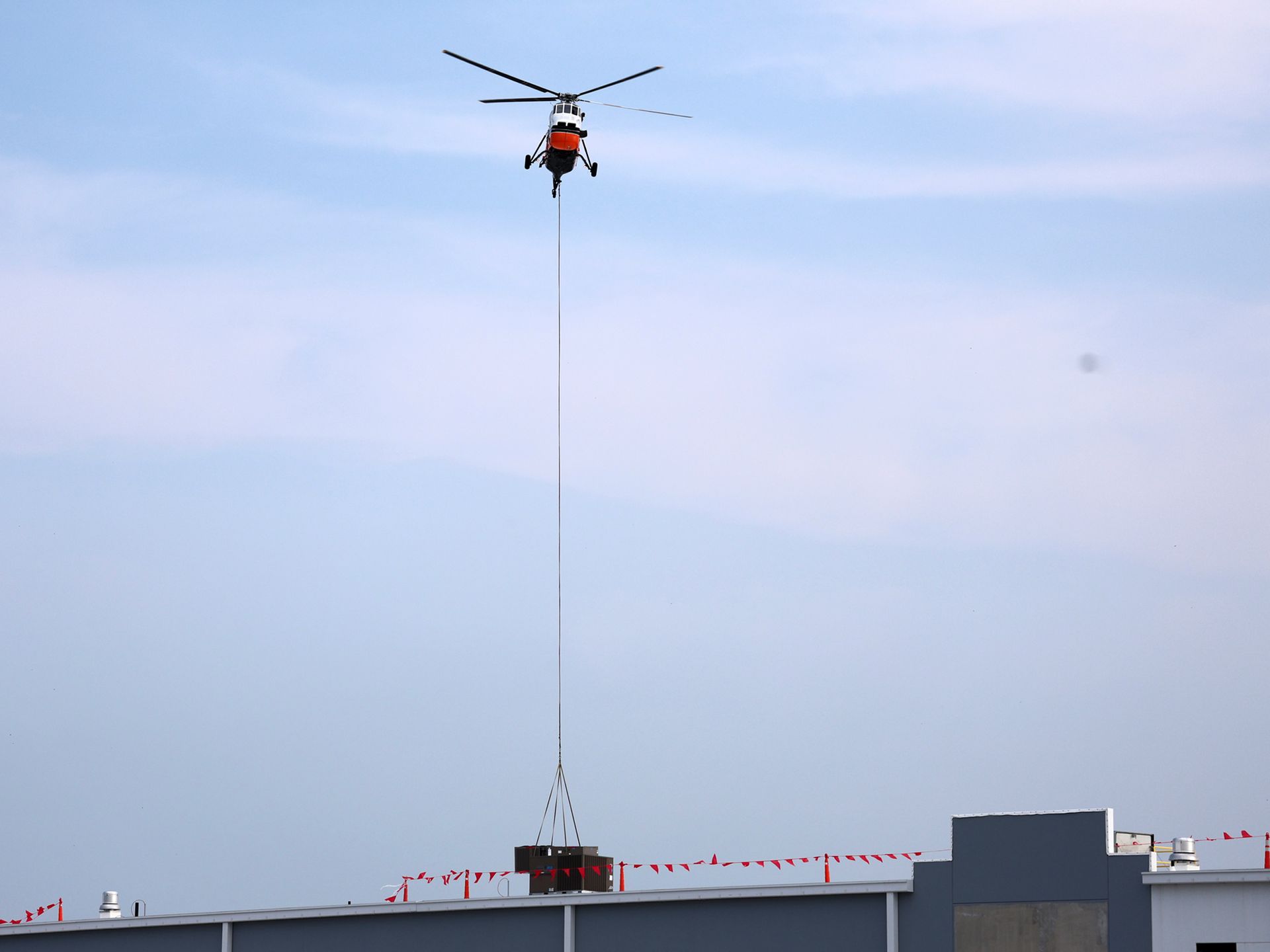 A helicopter is flying over a building with a crane attached to it