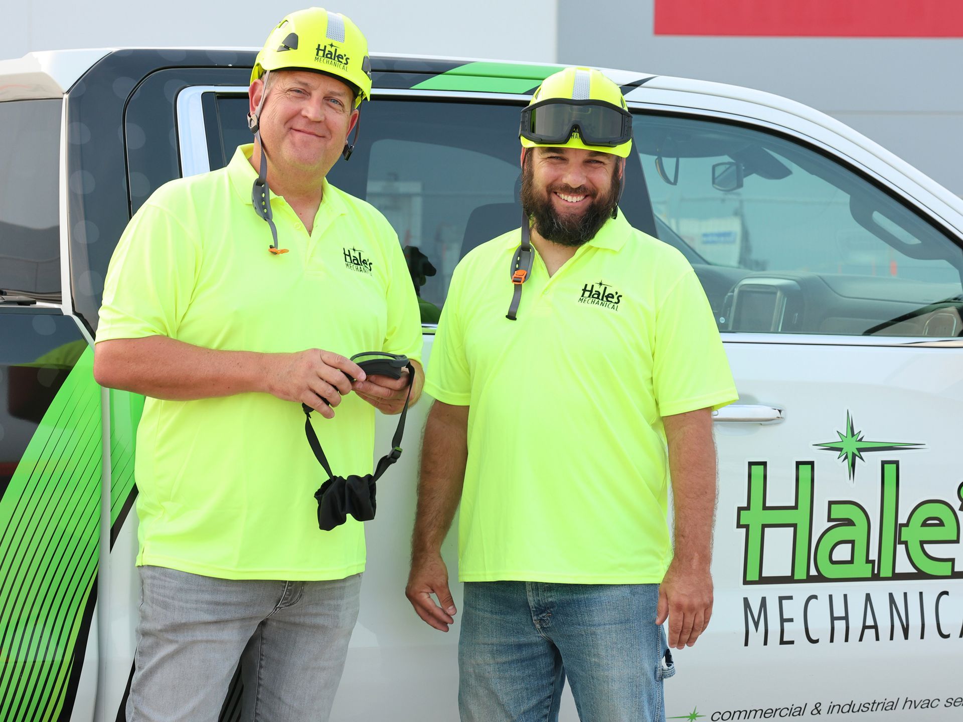 Two men wearing hard hats and goggles are standing next to a white van.