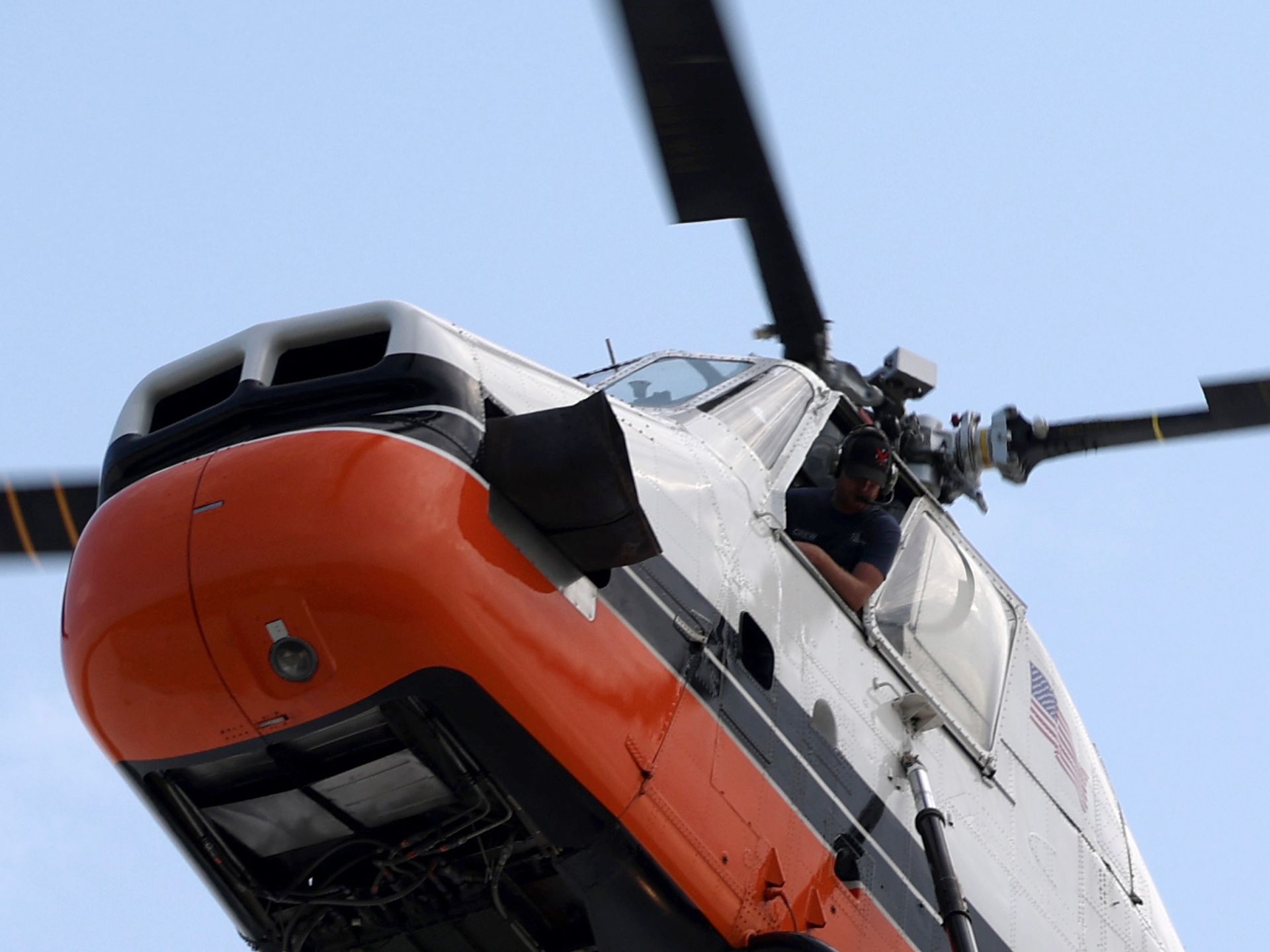 An orange and white helicopter is flying in the sky