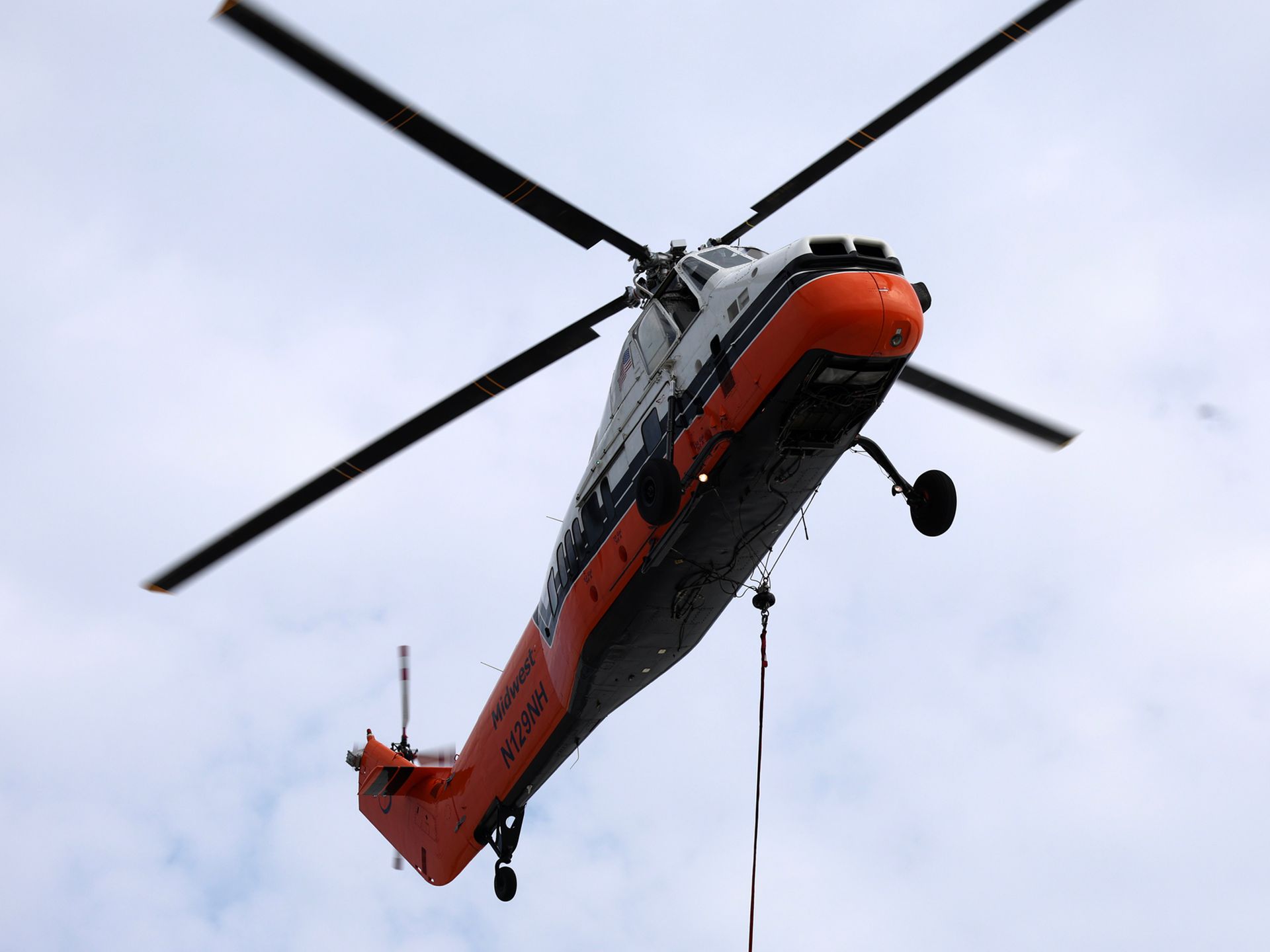 An orange and white helicopter is flying in the sky