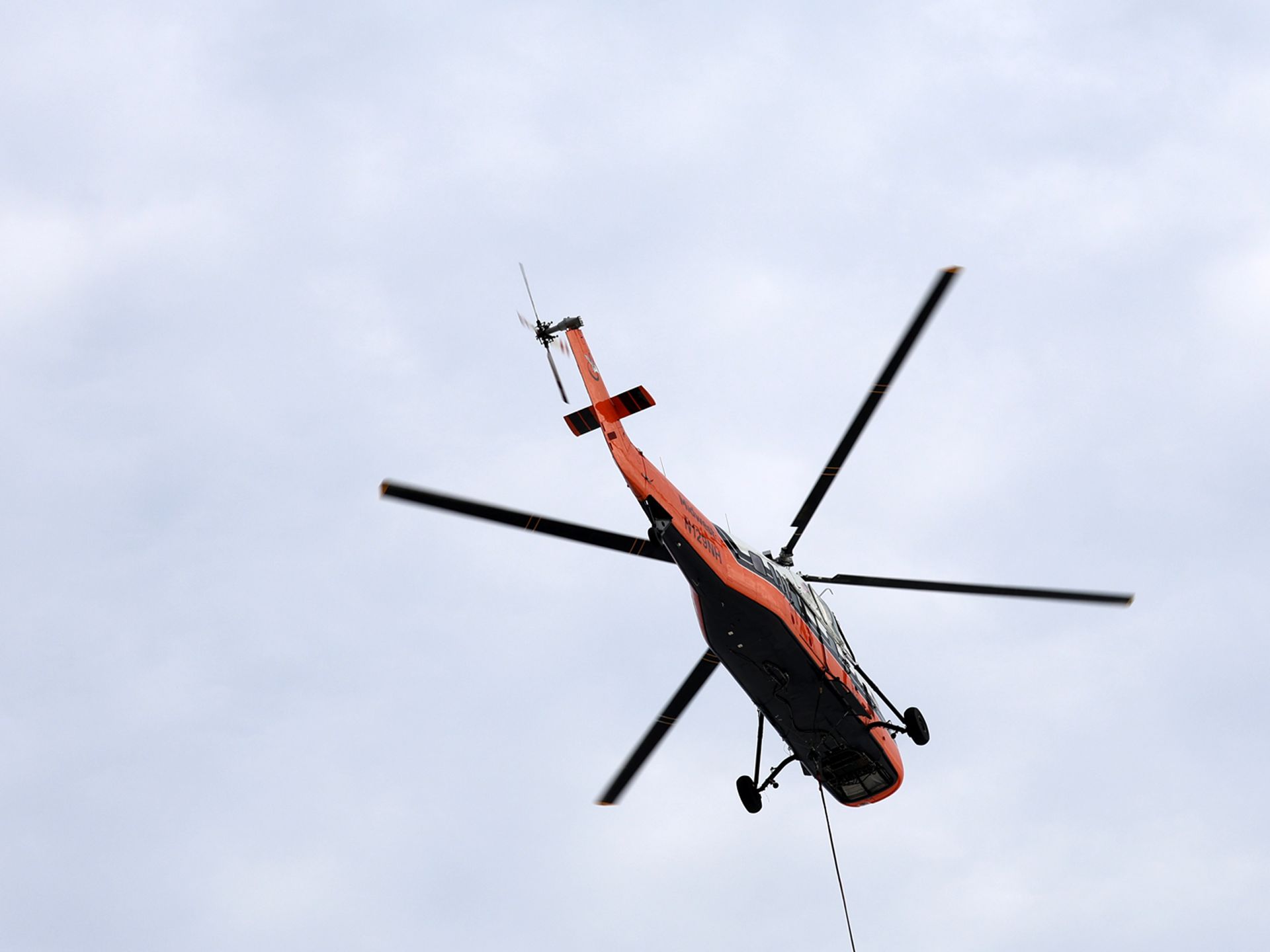 An orange and black helicopter is flying through a cloudy sky