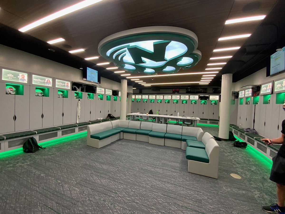 A man is standing in a locker room with green lights.