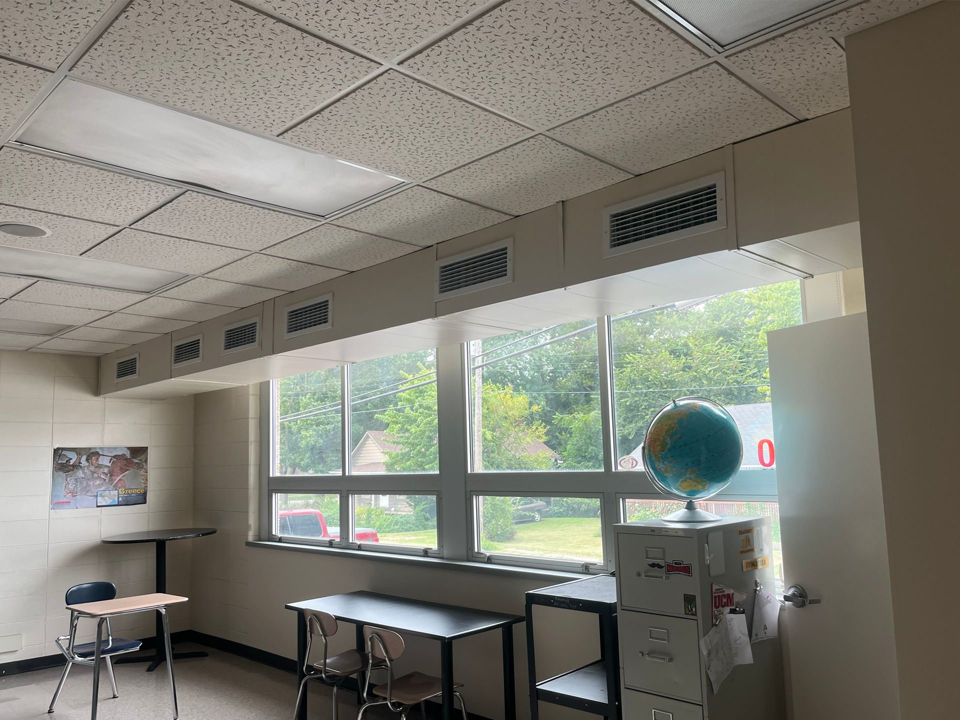 A classroom with tables , chairs , a globe and a filing cabinet.
