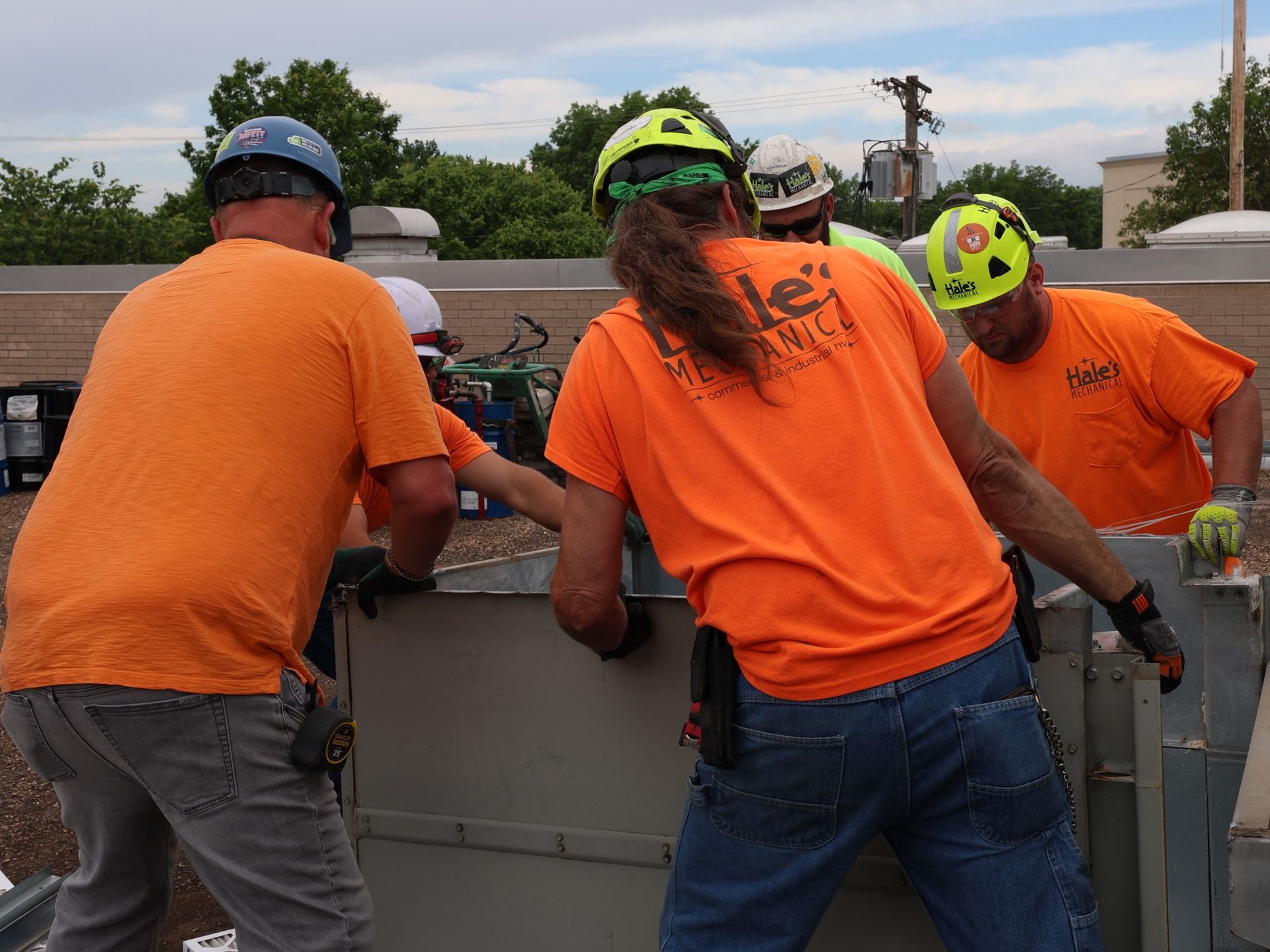 Construction workers wearing orange shirts and helmets, working on a rooftop.