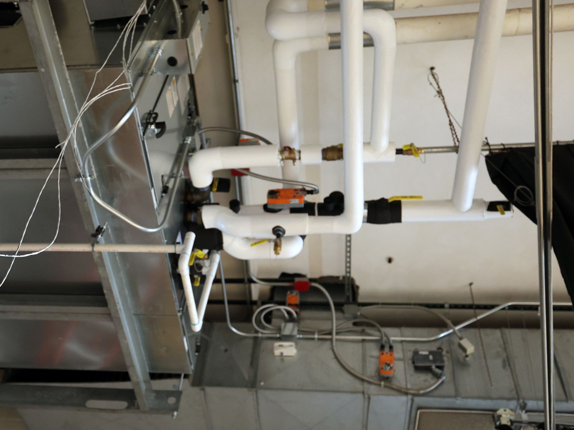Pipes and valves against a silver ceiling, part of an HVAC system.
