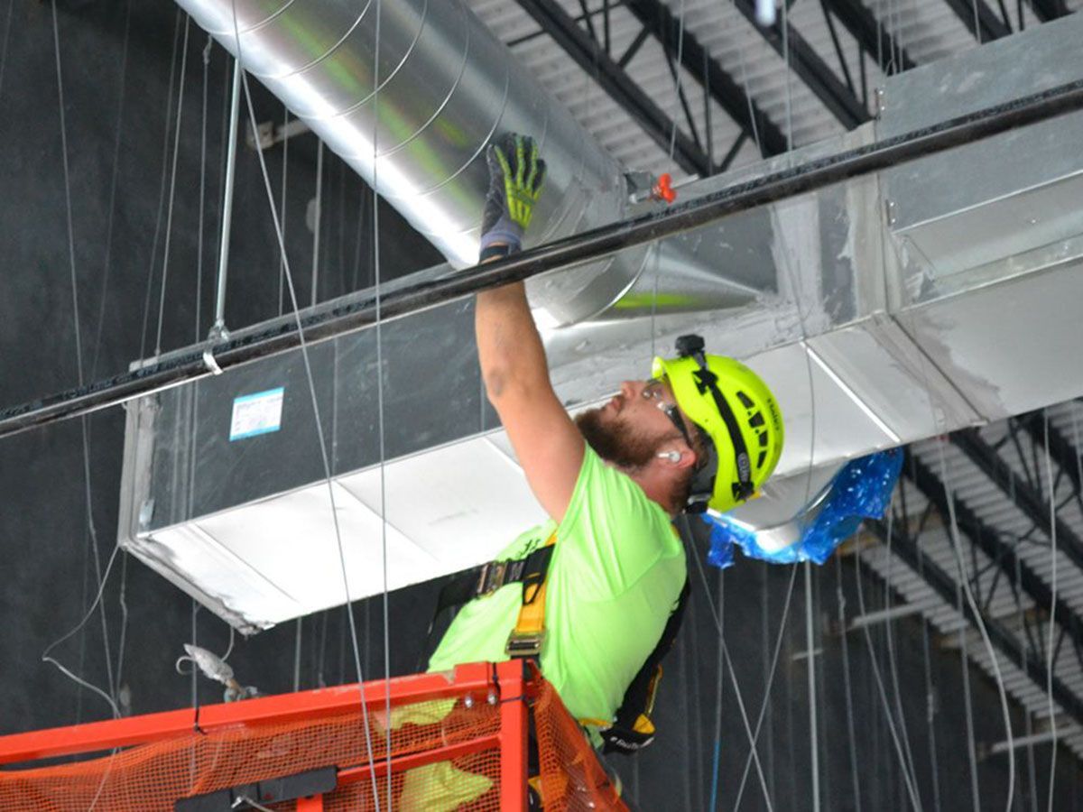 A man in a green shirt and safety helmet is working on an air duct