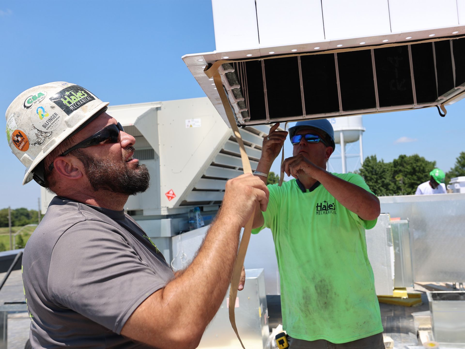 Two construction workers installing a panel on a rooftop, one holding a strap.