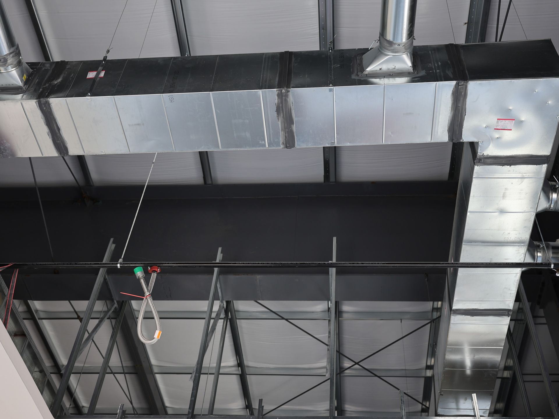 Galvanized metal air ducts running along ceiling. Black support beams and white insulation visible.