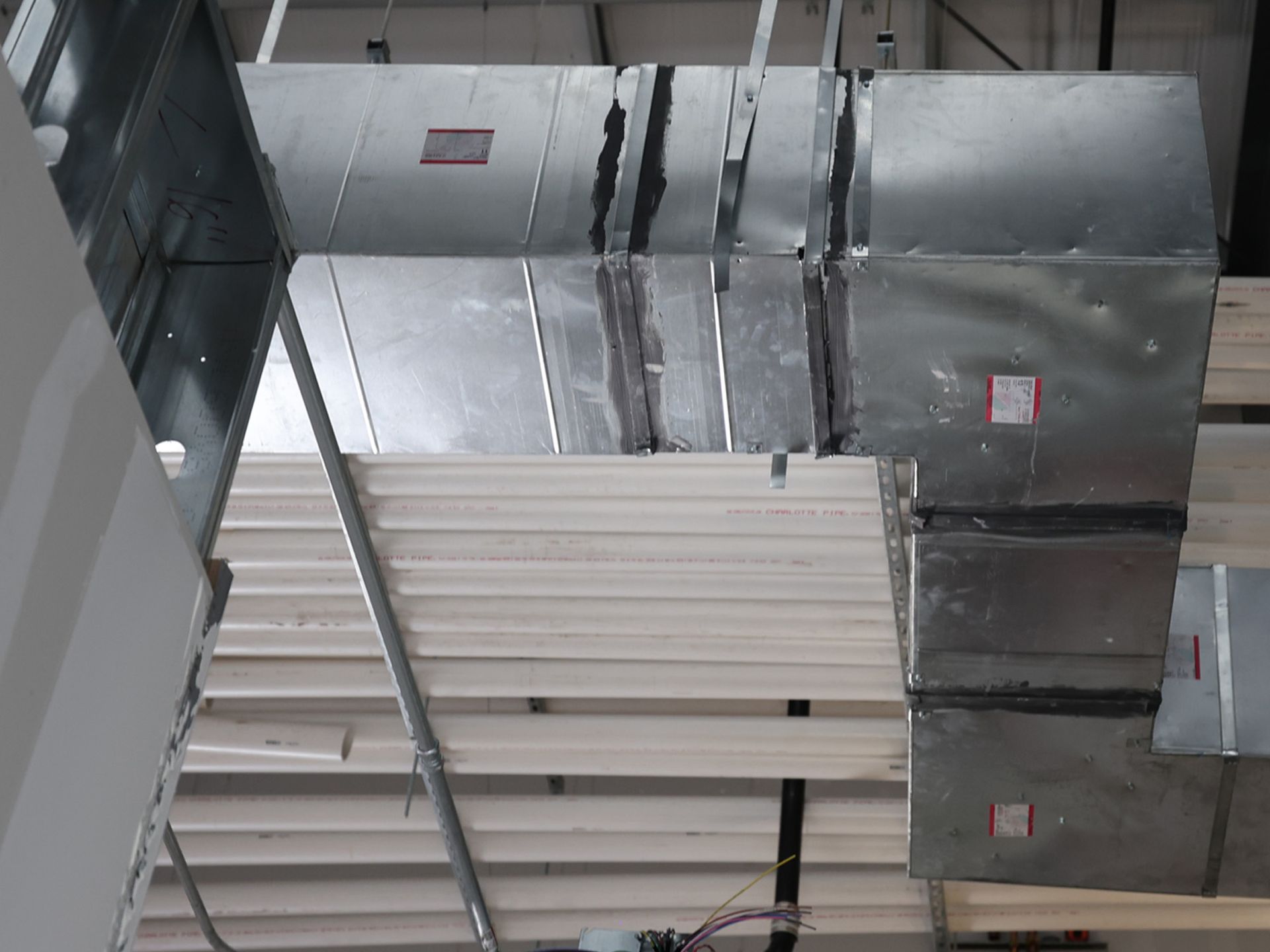 Metal ductwork running along a ceiling. The ductwork is rectangular and connected in an industrial setting.