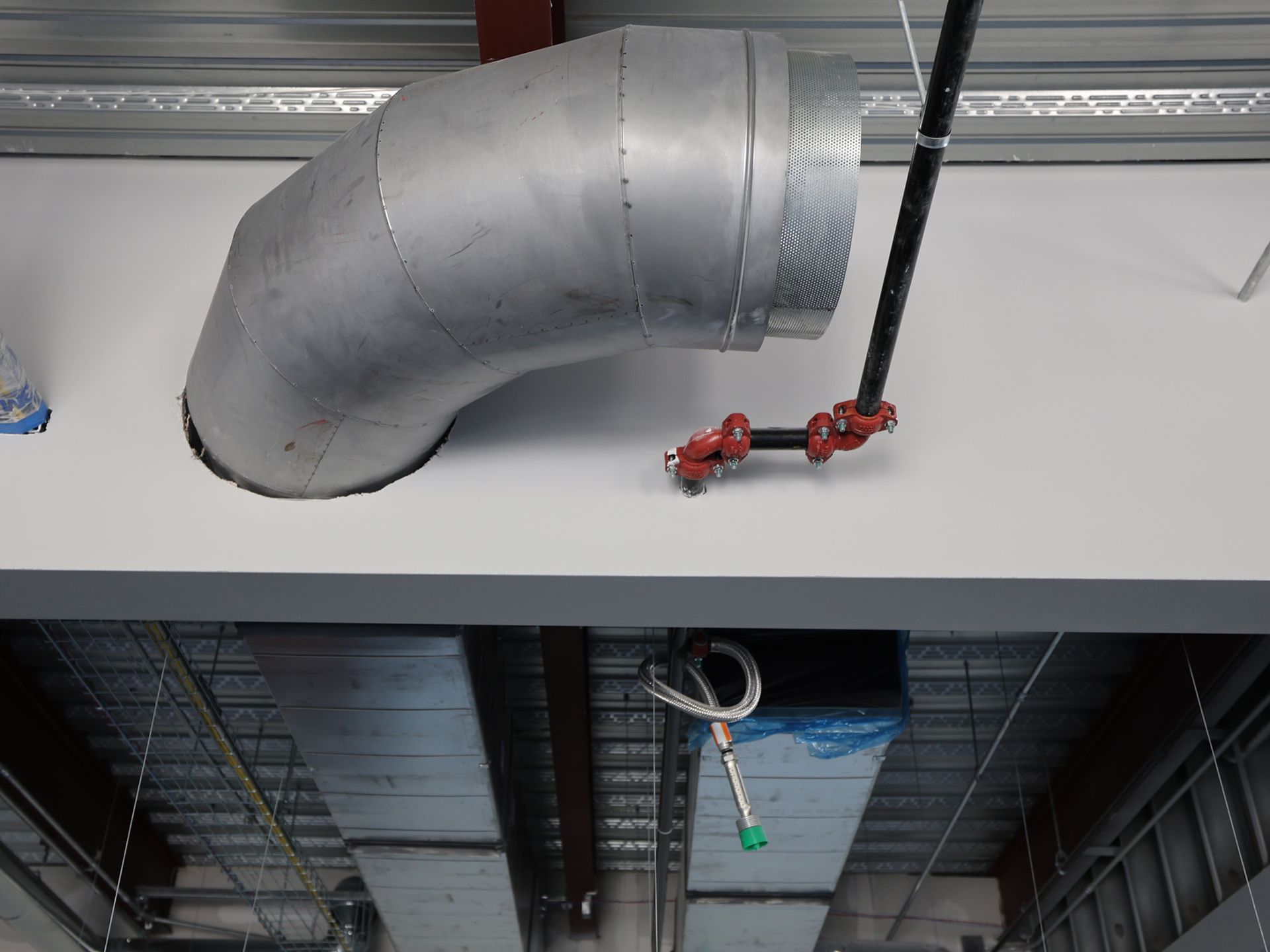Metal ductwork angled above a suspended ceiling; a black pipe and red fixtures are also visible.
