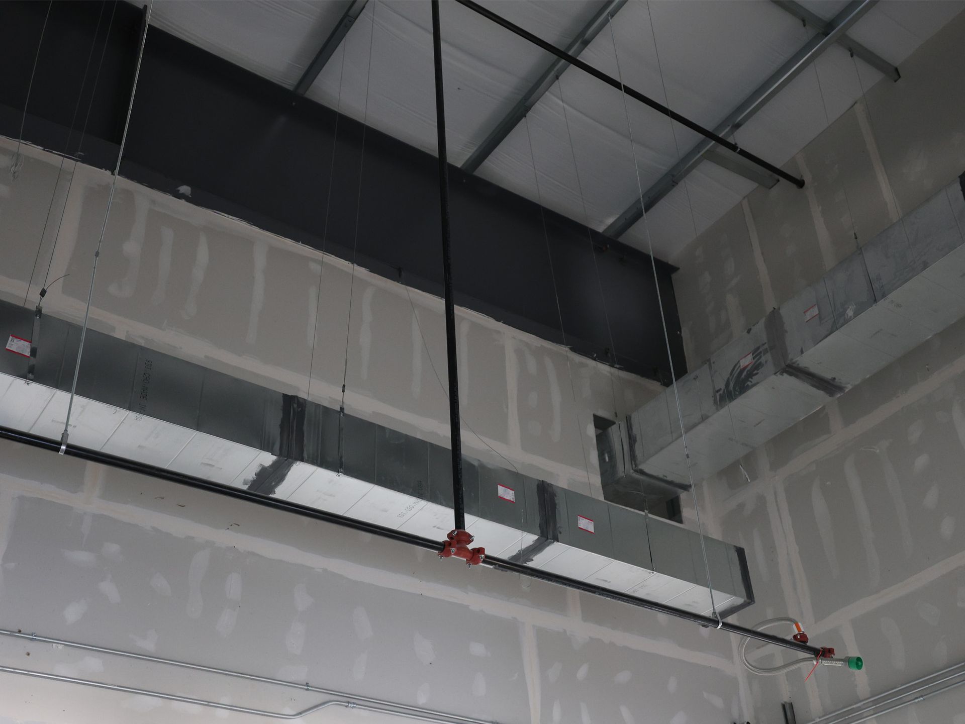 Ceiling of a construction site with HVAC ductwork, metal beams, and sprinkler system.