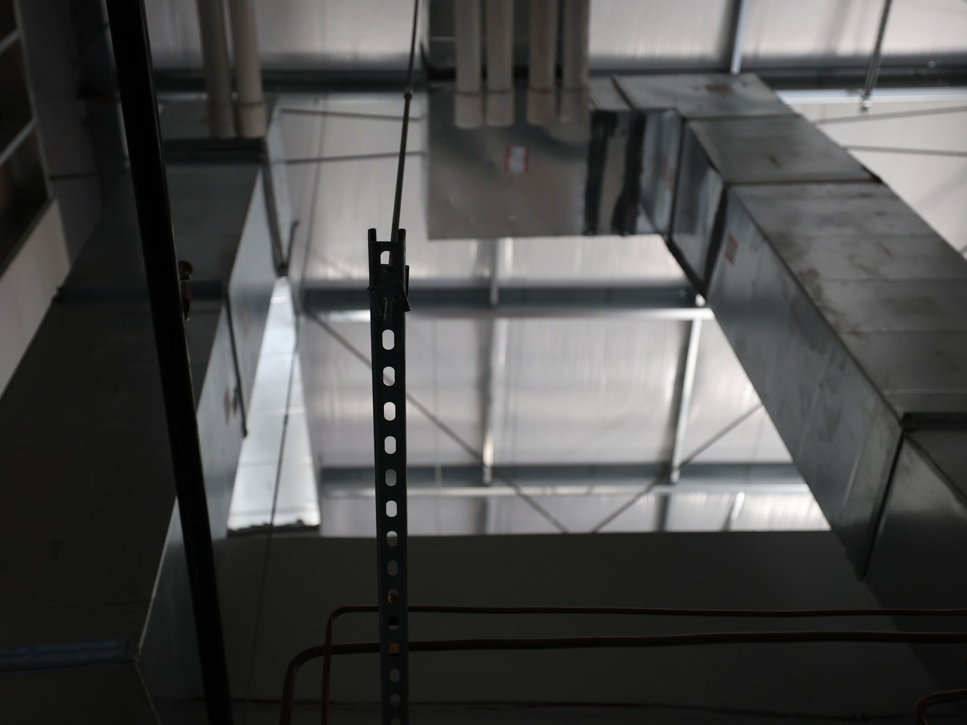 Metal ductwork and framework in a building's industrial ceiling. A vertical metal support hangs down.