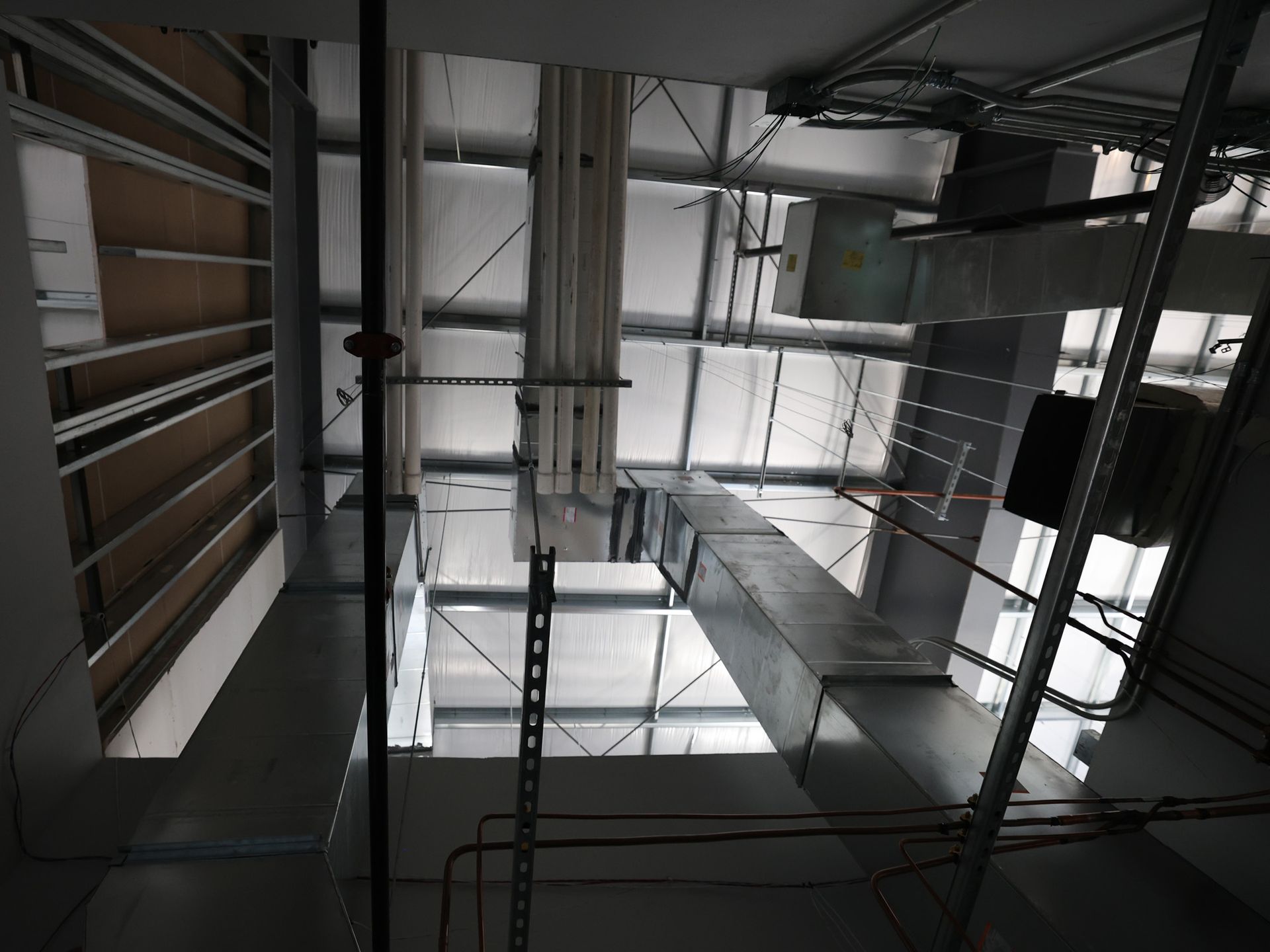 Overhead view of a building interior with exposed metal ductwork, pipes, and electrical wiring.