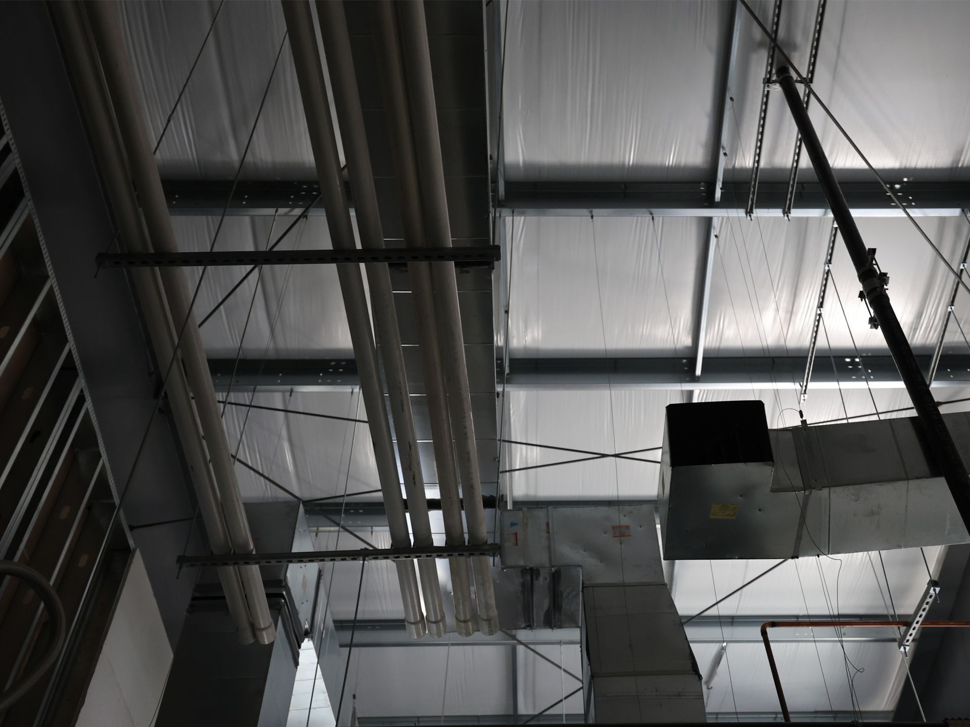 Industrial ceiling with pipes, metal beams, and ductwork.