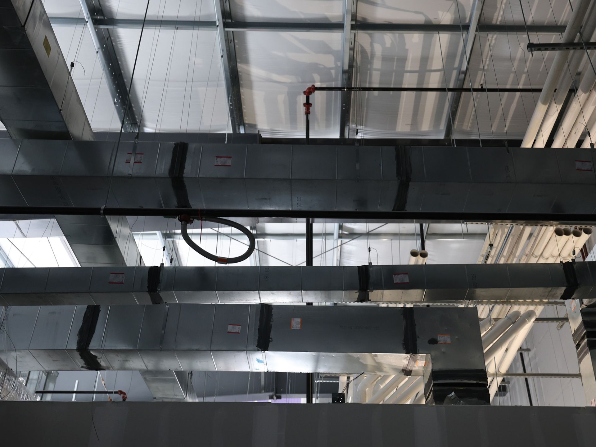 Ceiling view: metallic HVAC ducts and pipes suspended, with fluorescent lighting above.