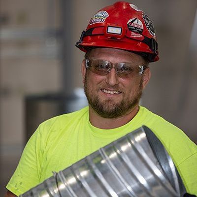 A man wearing a hard hat and sunglasses is holding a metal pipe.