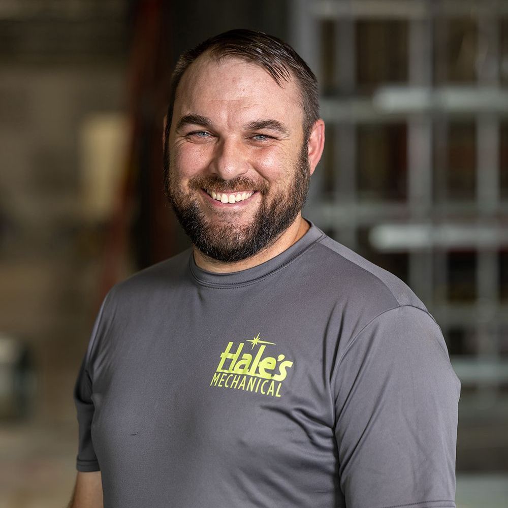 A man with a beard is wearing a gray shirt and smiling.