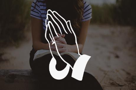 A woman is sitting on a bench with her hands folded in prayer.
