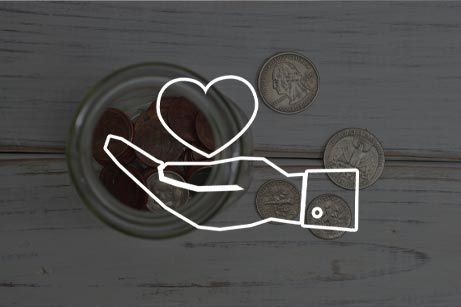 A hand is holding a heart in front of a jar of coins.