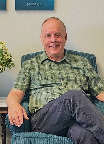 A man is sitting in a chair with his legs crossed and smiling.