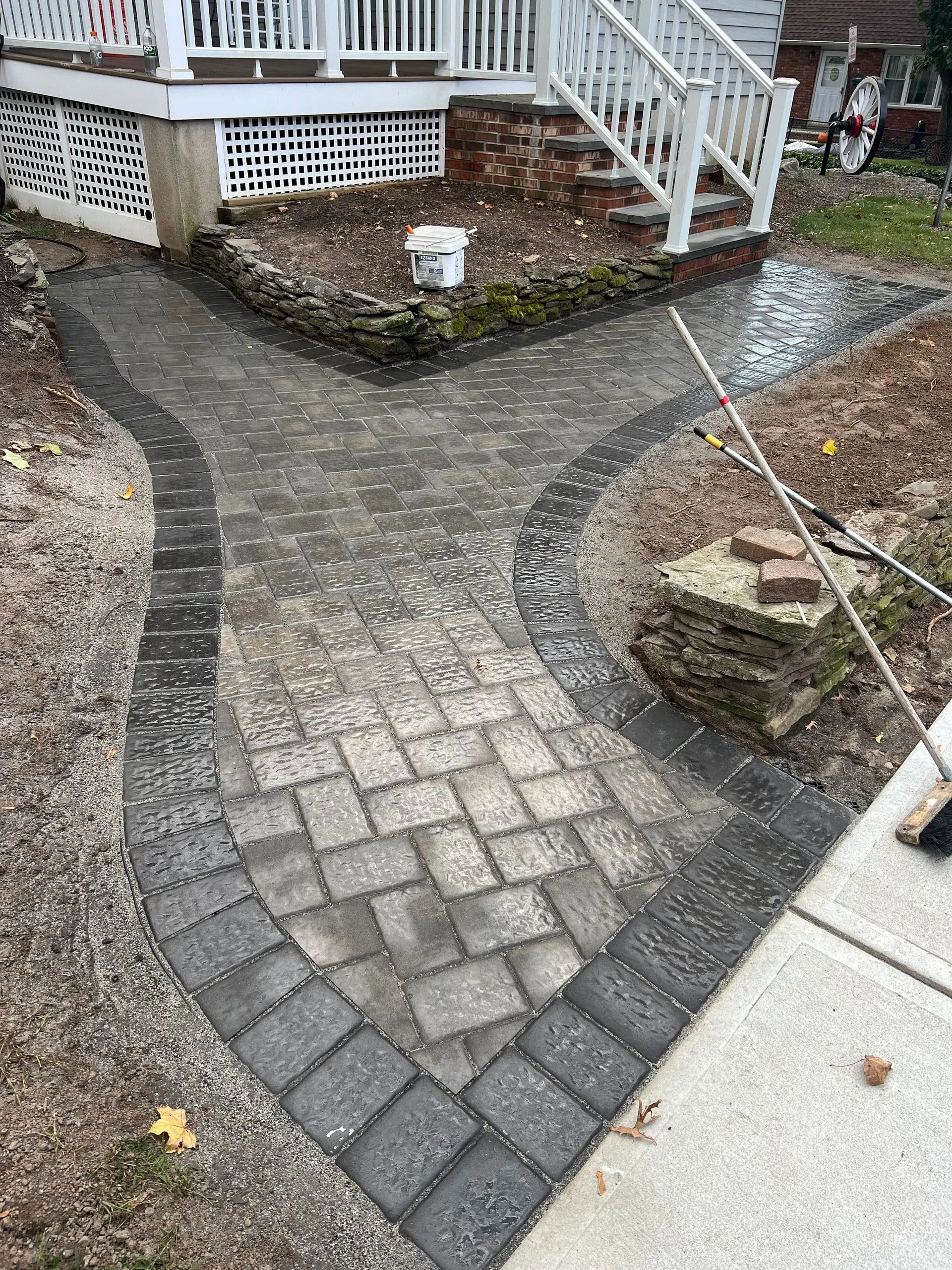 Brick pathway forks, leading to a porch and sidewalk. Gray pavers with dark border.