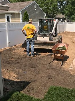 A man is standing in front of a bulldozer in a backyard.