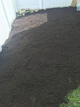 A pile of dirt is sitting on the ground next to a white fence.