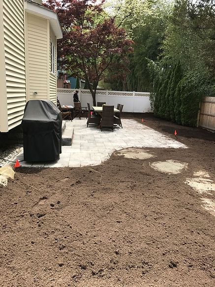 A backyard with a patio and a house in the background.