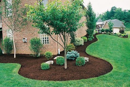 A brick house with a lush green lawn and trees in front of it.