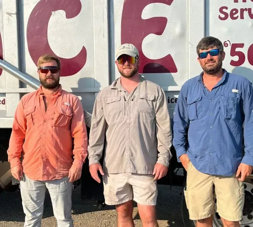Three people wearing sunglasses and button-down shirts stand side-by-side in front of a white truck with red lettering.