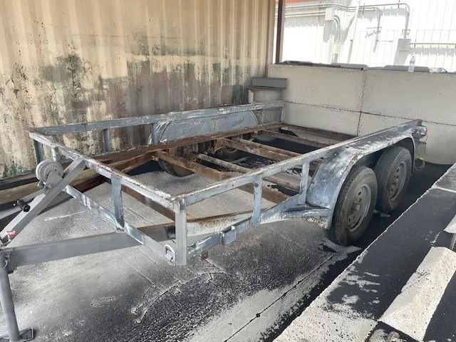 A rusty utility trailer with two wheels, in an industrial setting.