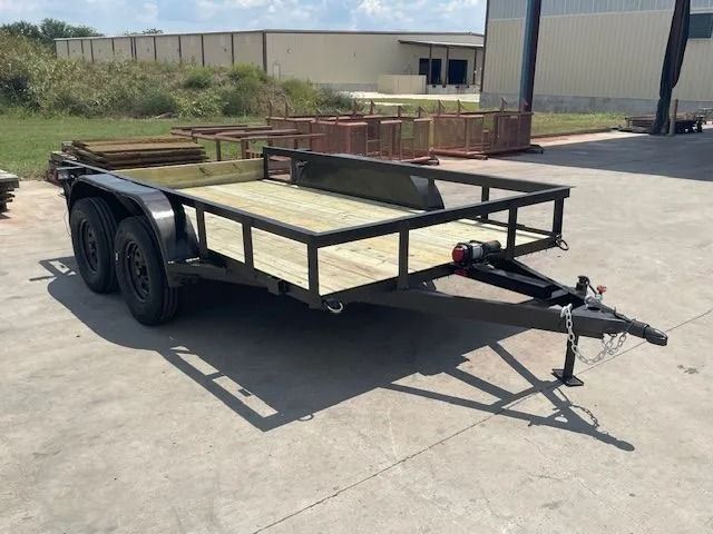 Black utility trailer with wooden deck, parked on concrete.