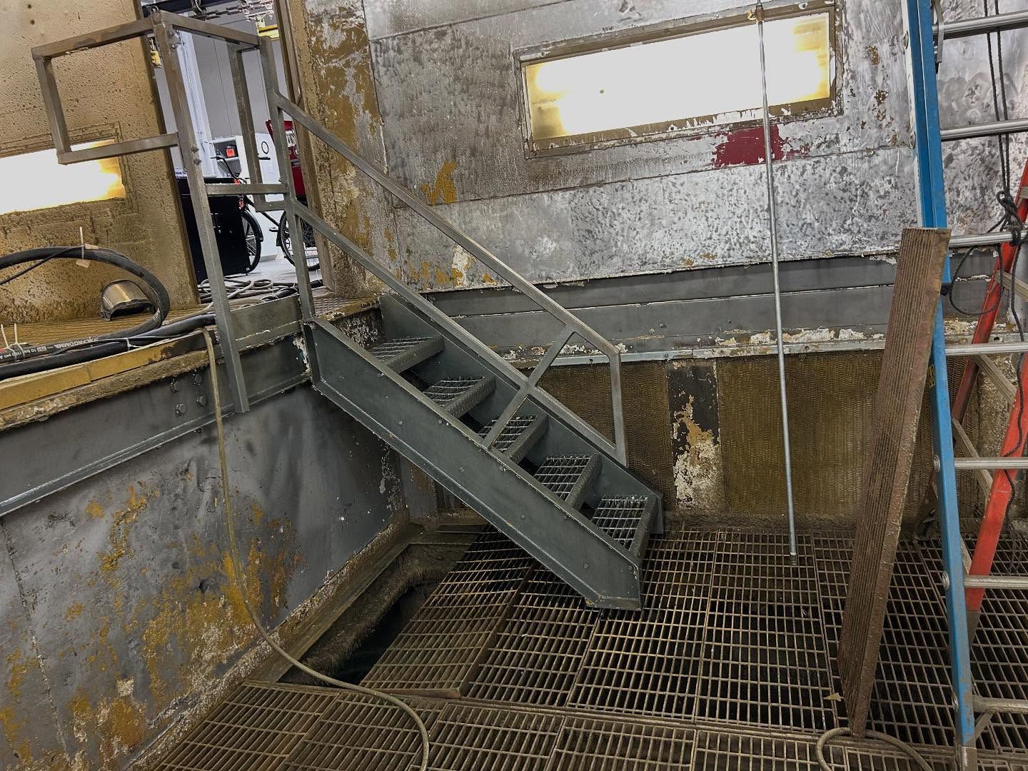 Metal stairs leading down into a grimy industrial pit. The walls are stained.
