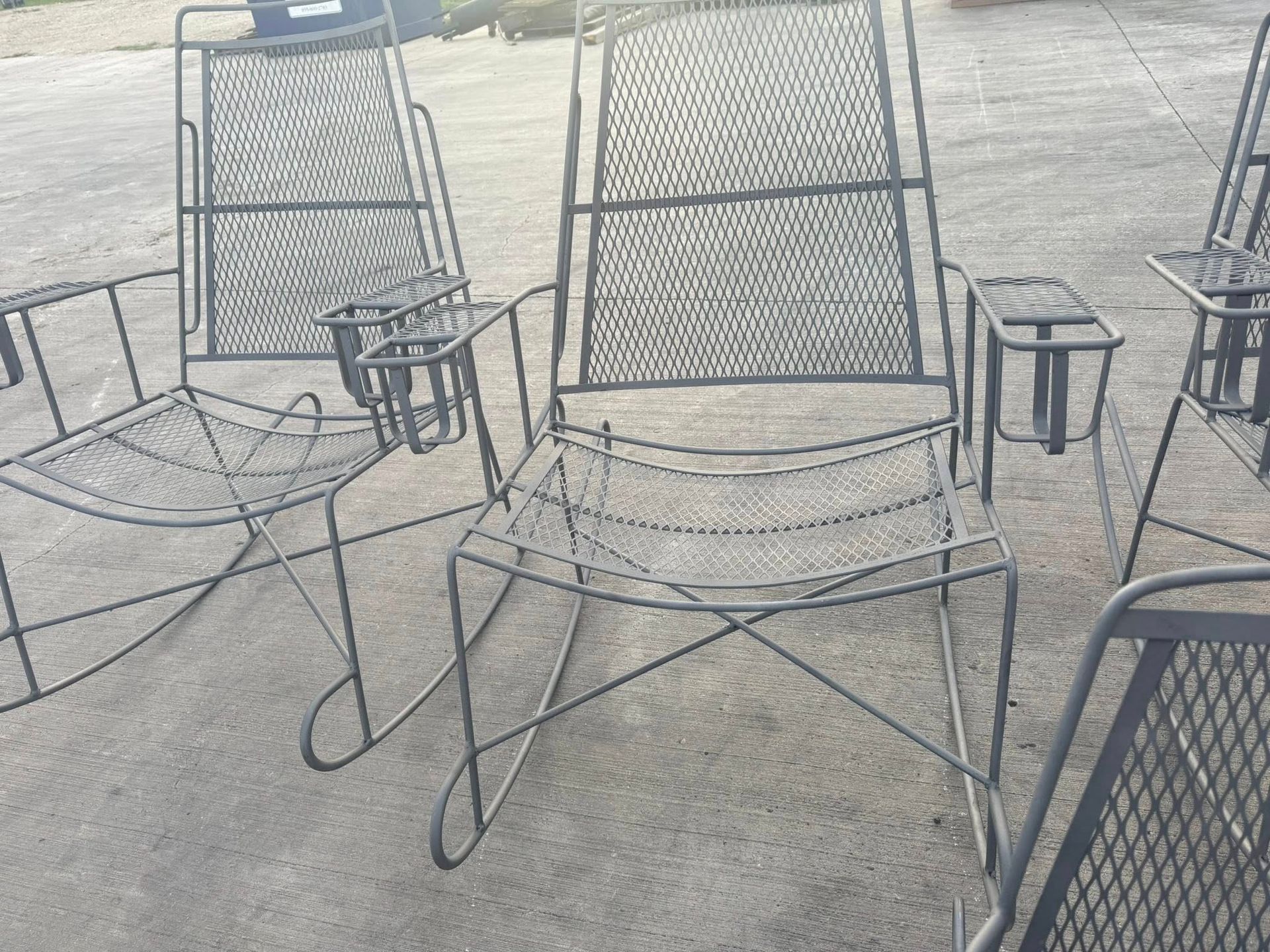 Black metal rocking chairs with mesh seats and attached side tables on pavement.