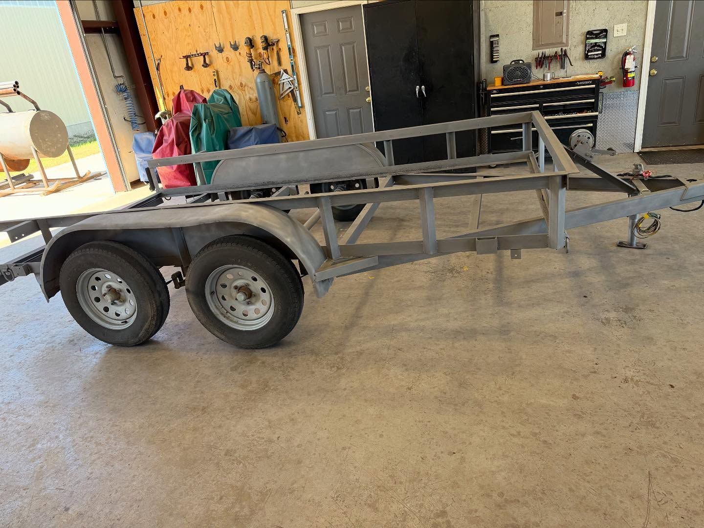 Gray trailer frame with two wheels in a workshop setting.